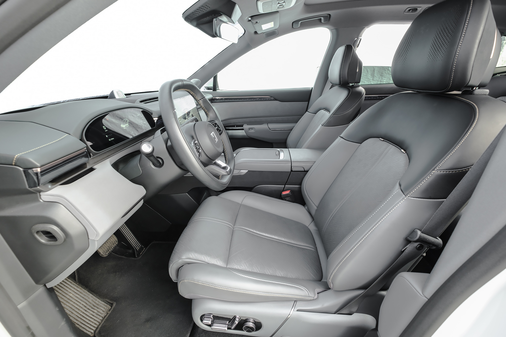 Interior de carro moderno com bancos de couro cinza e preto, painel escuro com tela digital, volante multifuncional e console central. Detalhes de costura branca nos assentos e acabamentos cromados. O cinto de segurança está visível no banco do passageiro