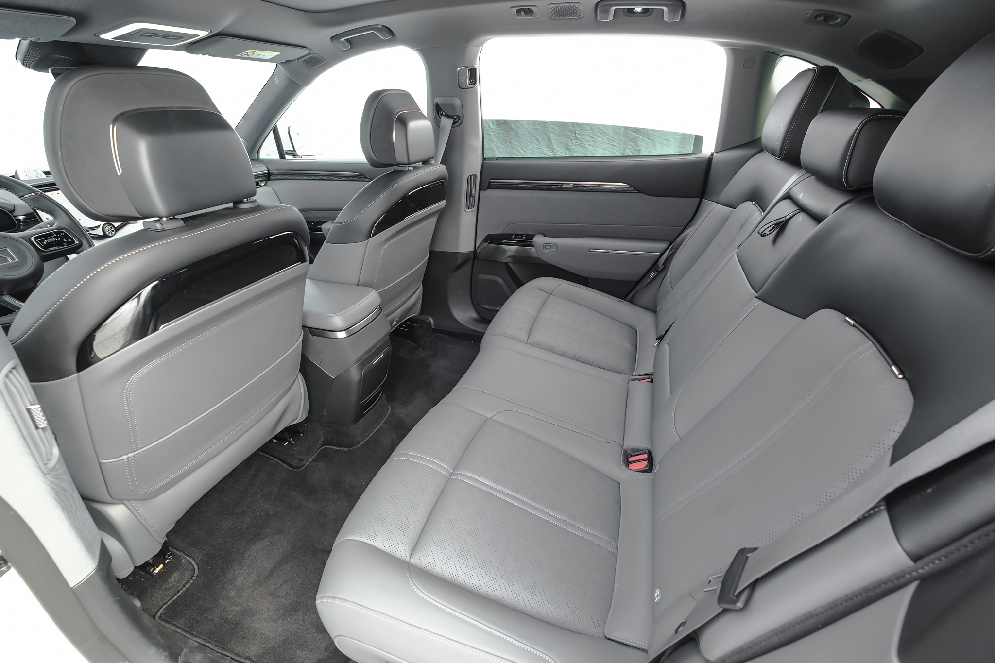 Interior de carro com bancos traseiros de couro cinza claro e detalhes em preto, vistos de um ângulo que mostra o espaço para as pernas e os encostos dos bancos dianteiros com acabamento brilhante