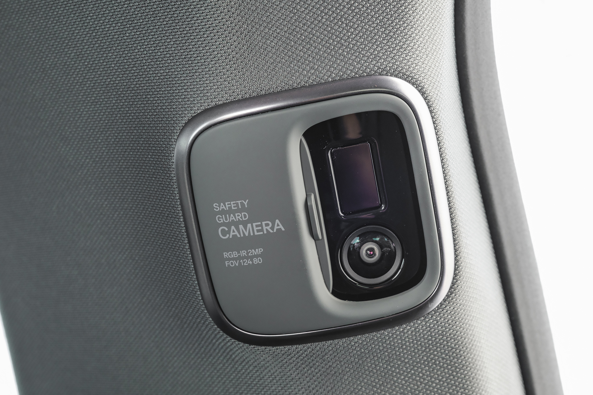 Câmera de segurança automotiva cinza, com lentes visíveis e texto SAFETY GUARD CAMERA RGB-IR 2MP FOV 124 80, instalada no pilar do carro, com tecido cinza texturizado ao redor