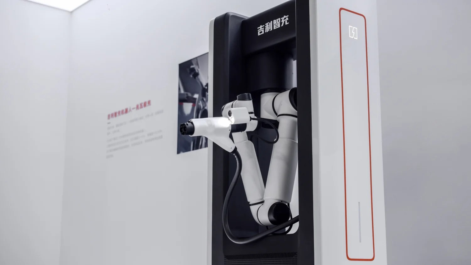 Braço robótico branco e preto com conector de carregamento de veículo elétrico, acoplado a uma estação de carregamento preta e branca com texto em chinês e um display retangular com um ícone de bateria