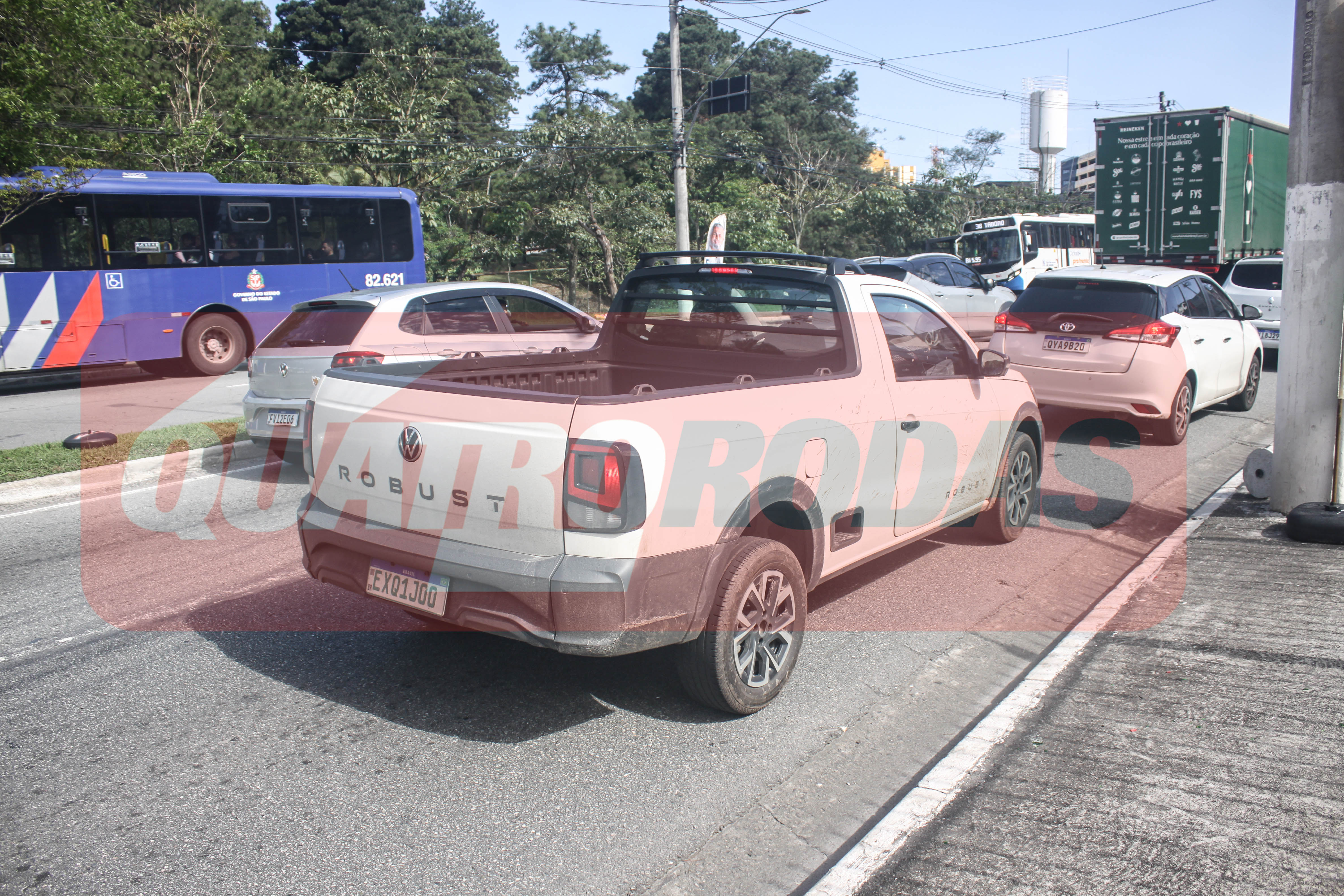 Uma picape branca Volkswagen Robust parada no acostamento de uma rodovia, com um ônibus azul e carros brancos atrás, em um dia ensolarado