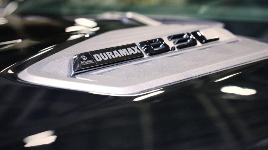 Detalhe do capô de um carro preto com um emblema prateado e preto que diz DURAMAX e 3500 em relevo, refletindo luzes