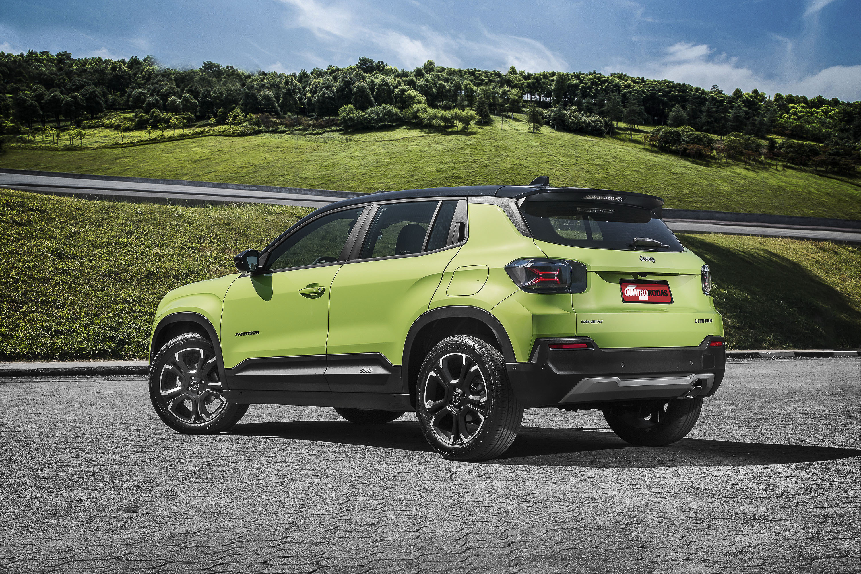 SUV Jeep Avenger verde-limão com teto preto, estacionado em uma área pavimentada. Ao fundo, uma estrada curva e colinas gramadas com árvores sob céu azul