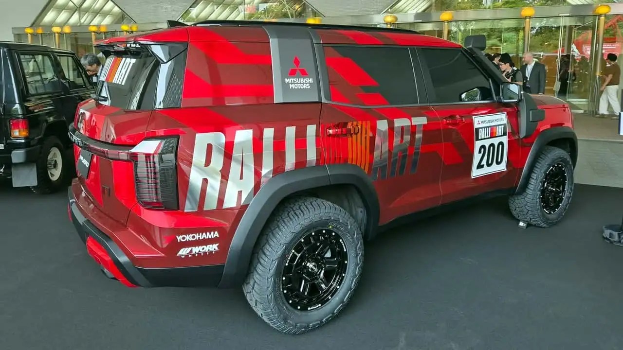 SUV Mitsubishi Ralliart vermelho com detalhes em preto e grafismos cinza, pneus off-road e número 200 na lateral, exibido em um evento com pessoas ao fundo