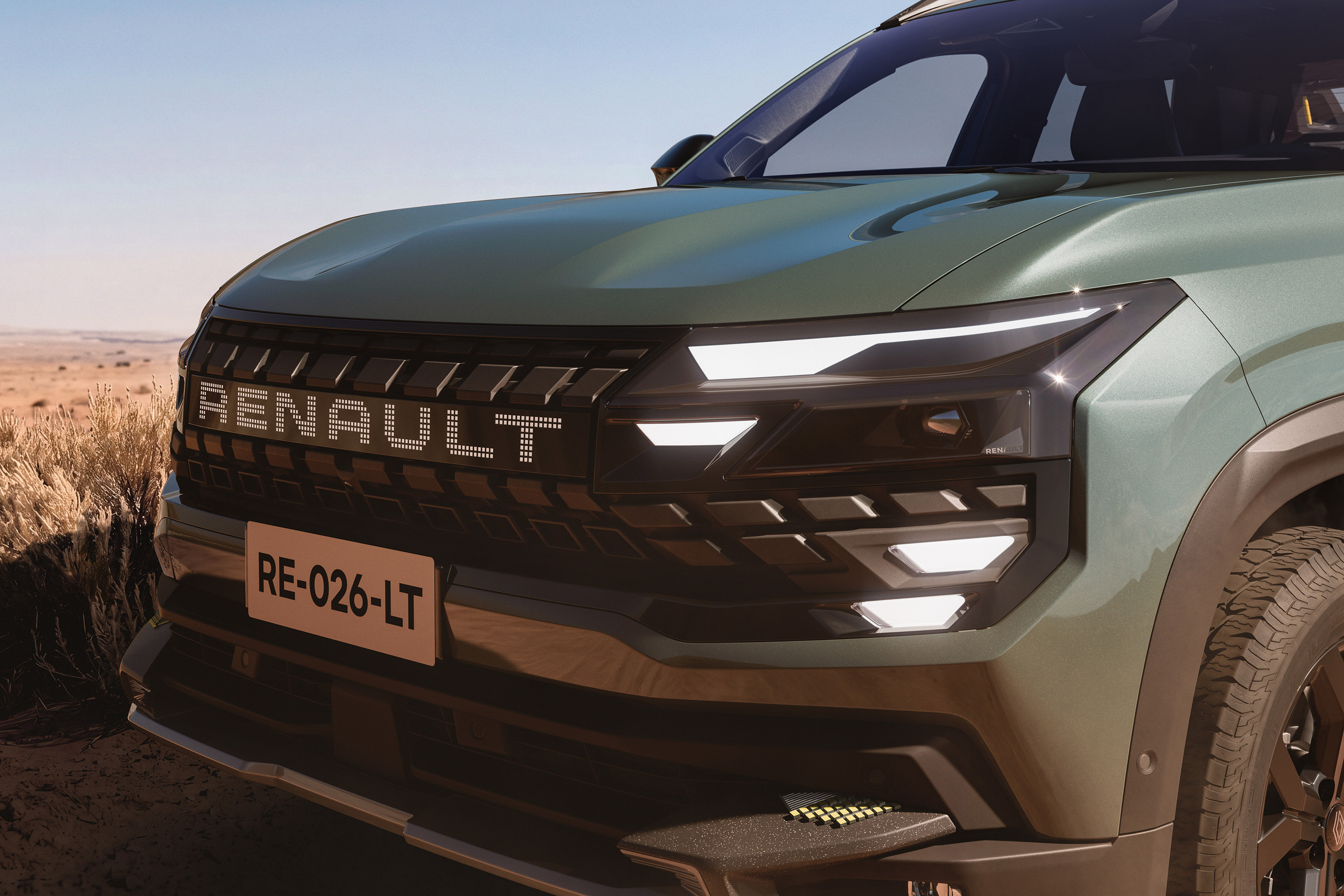 Frente de um carro Renault verde-oliva com faróis e luzes diurnas acesas, grade preta com o nome RENAULT em letras brancas e placa RE-026-LT, em cenário desértico