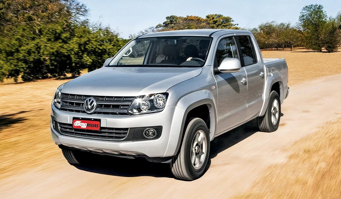 Picape Volkswagen Amarok prata em movimento, vista de frente e levemente de lado, em uma estrada de terra com vegetação ao fundo