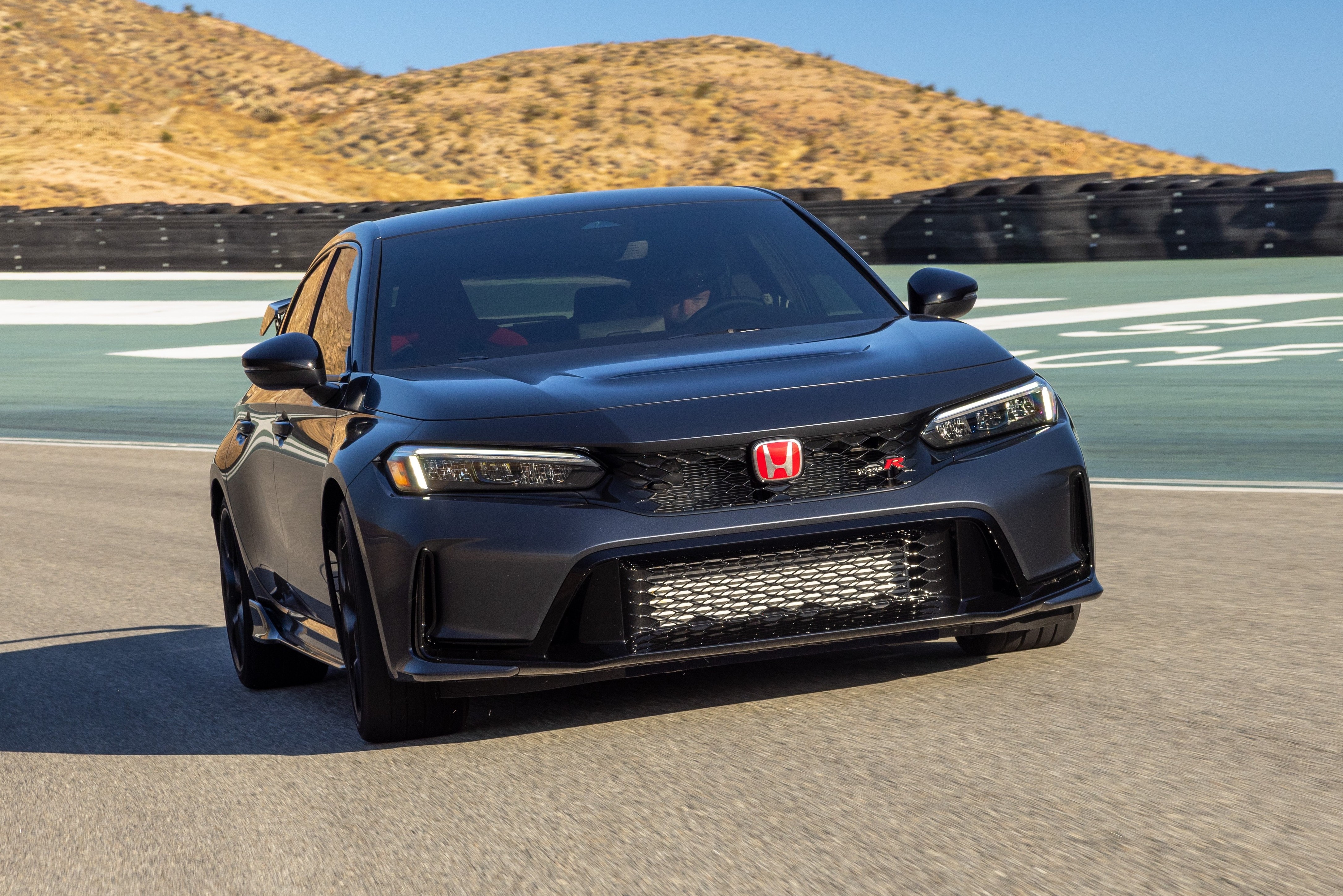 Carro esportivo Honda Civic Type R cinza-escuro em uma pista de corrida, com montanhas áridas ao fundo