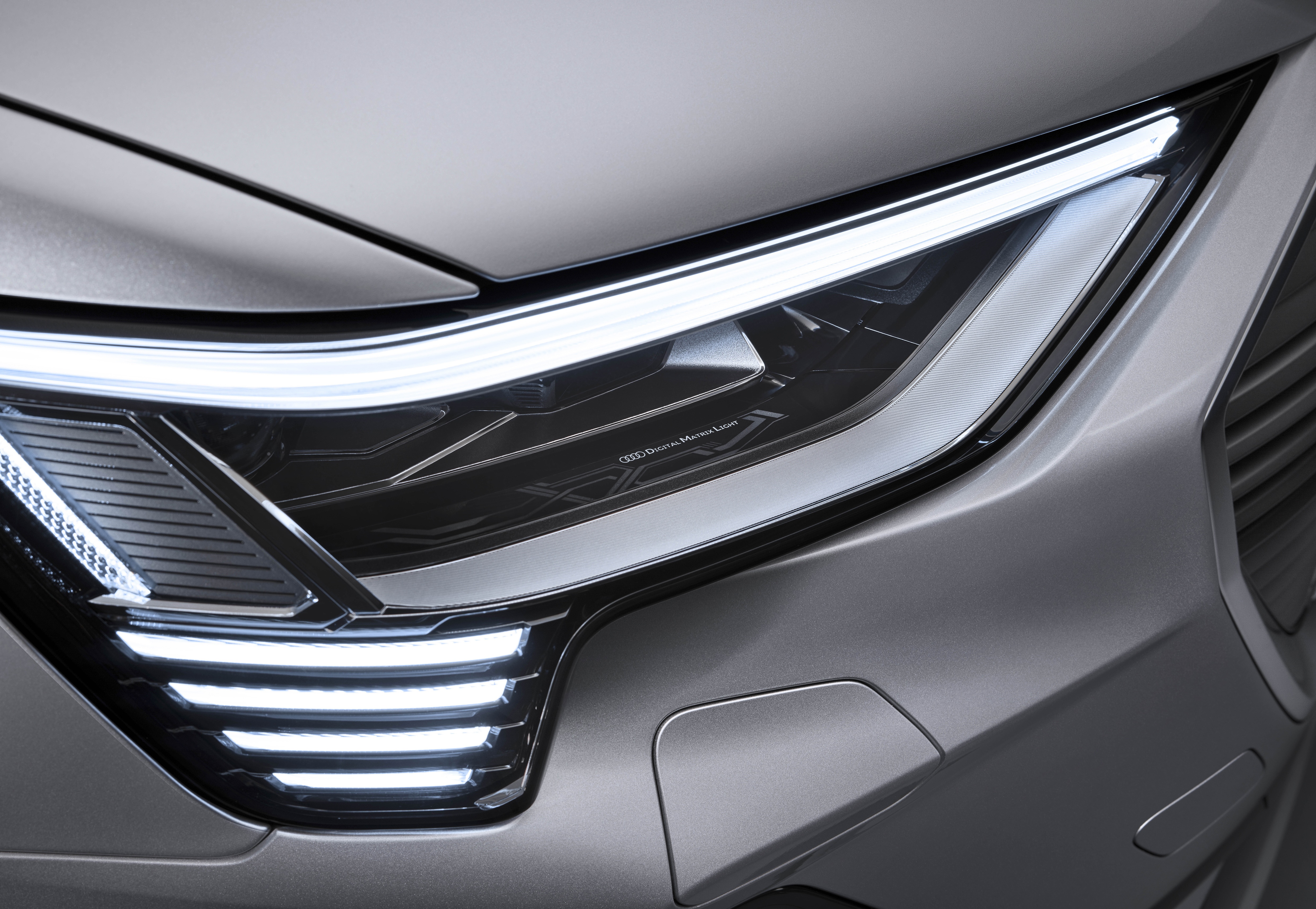 Farol de LED aceso de um carro cinza, com uma linha horizontal superior e quatro barras verticais inferiores brilhantes