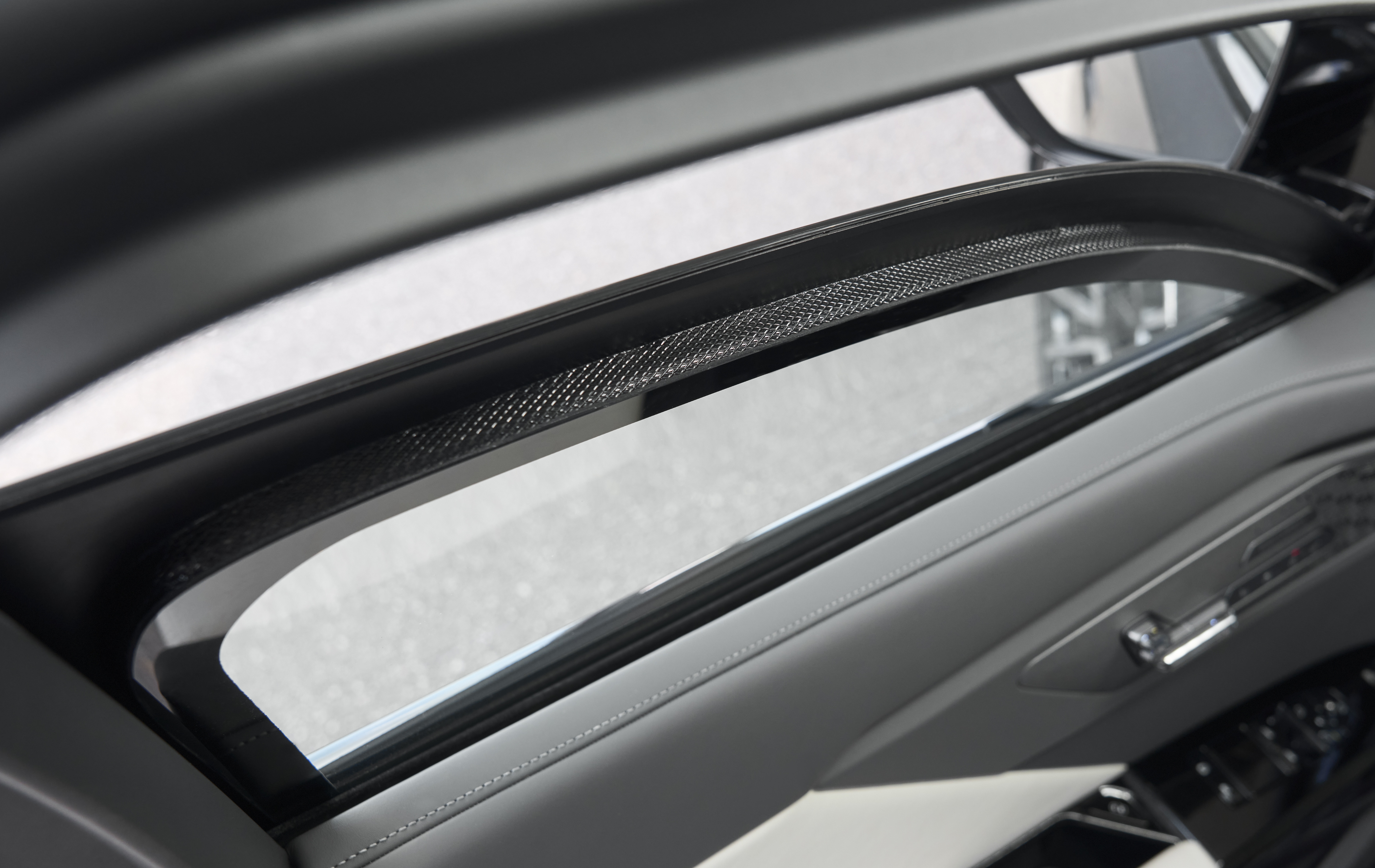 Teto solar de um carro, com a parte interna em cinza claro e detalhes em preto texturizado, refletindo o asfalto lá fora