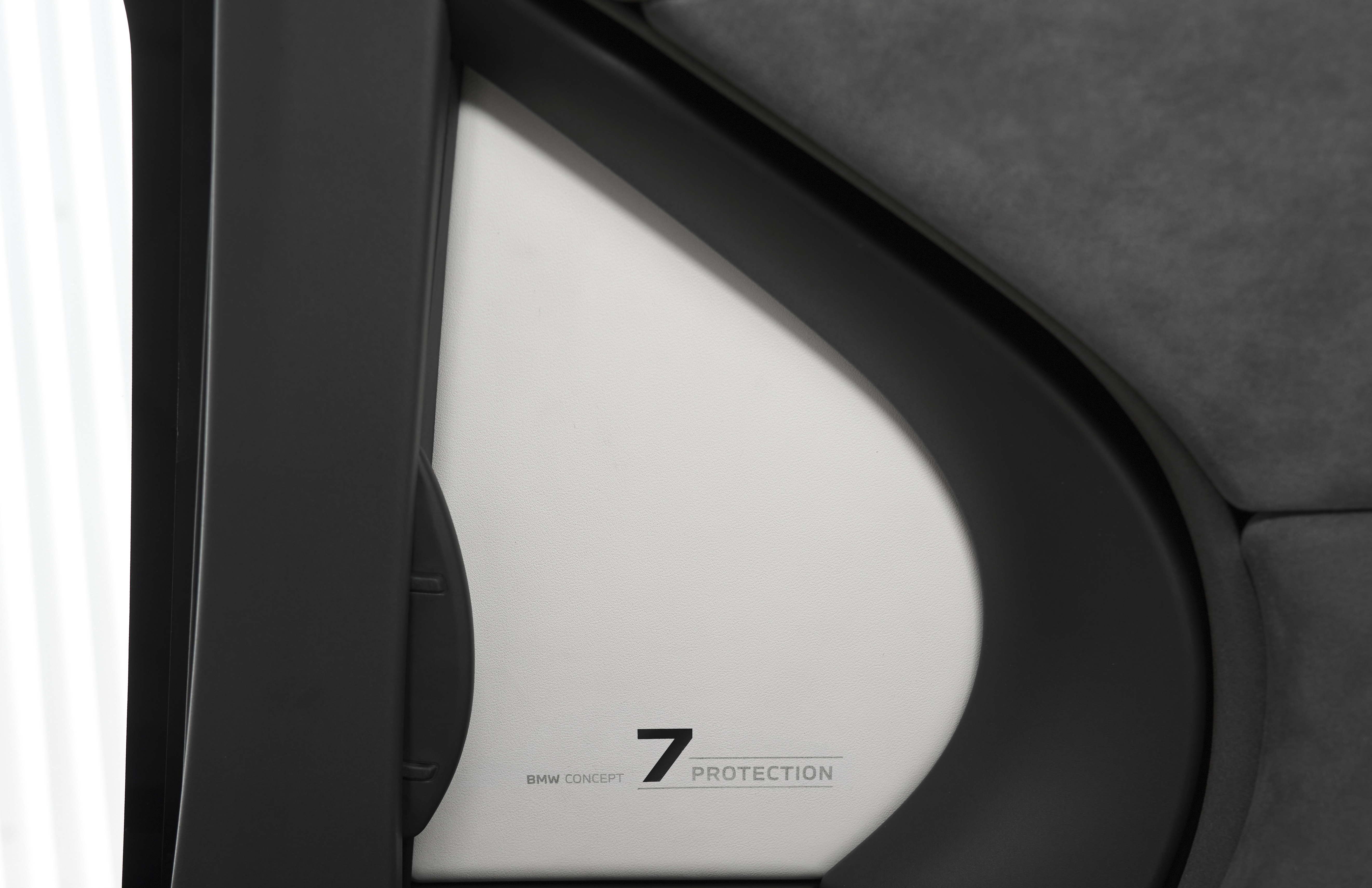 Detalhe do interior de um carro, mostrando uma superfície branca com o texto BMW CONCEPT 7 PROTECTION em preto, emoldurada por acabamentos escuros e estofamento cinza no canto superior direito