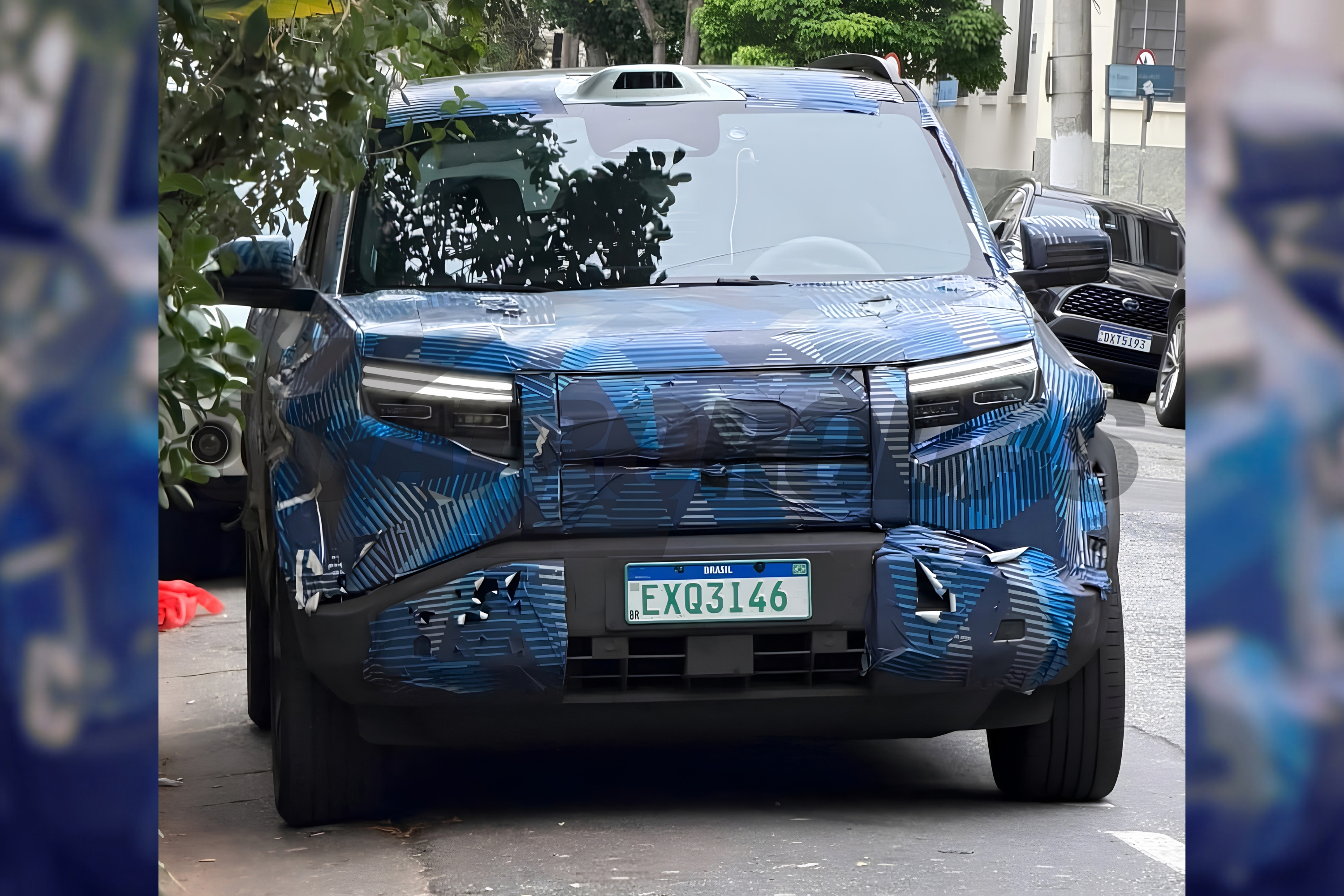 Um carro camuflado com adesivos azuis e pretos, com faróis de LED acesos, parado em uma rua. A placa verde e branca exibe EXQ3I46.