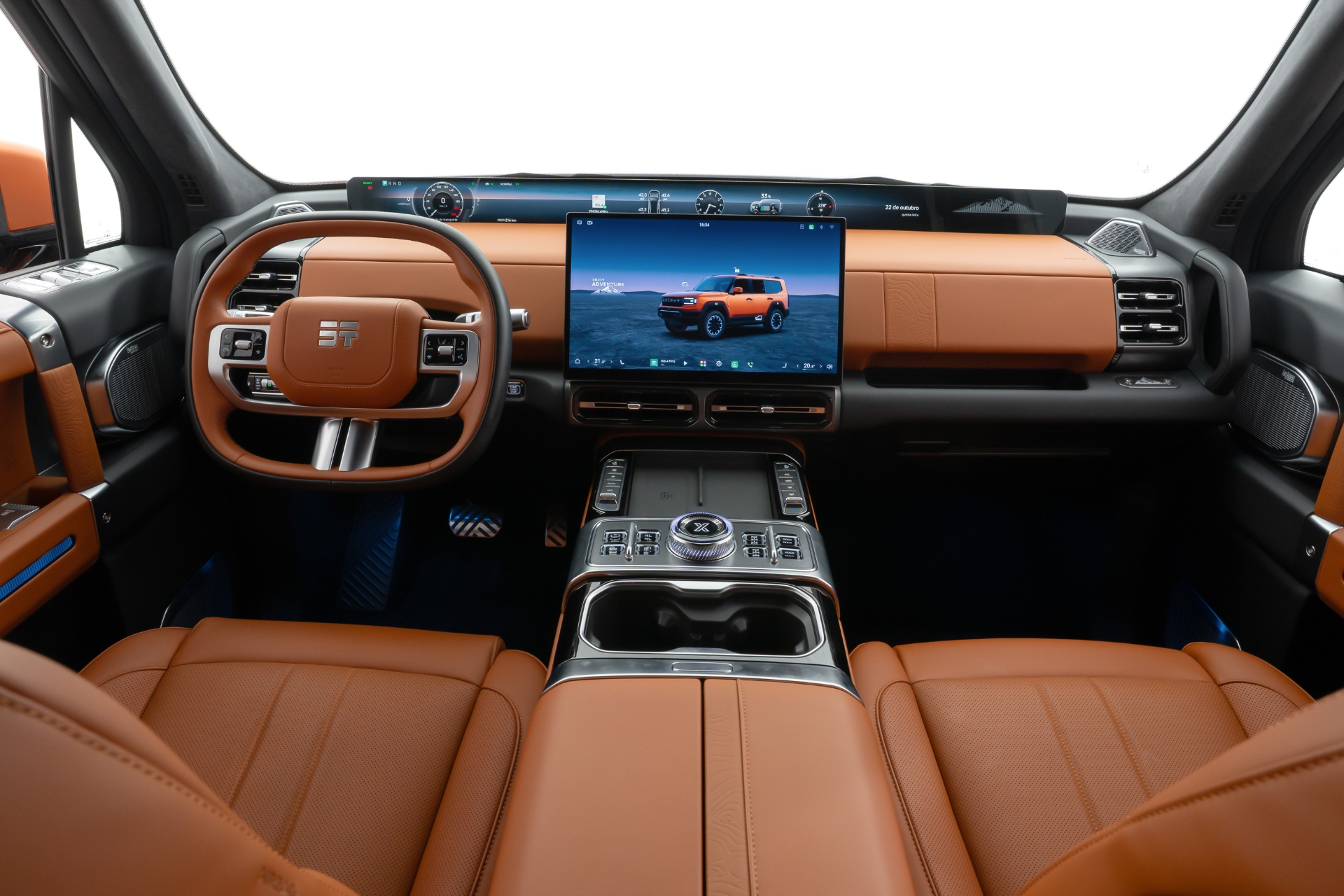 Interior de um carro moderno com bancos de couro marrom, volante marrom e painel digital. Uma tela central exibe um SUV laranja em paisagem desértica. O console central possui botões e porta-copos.