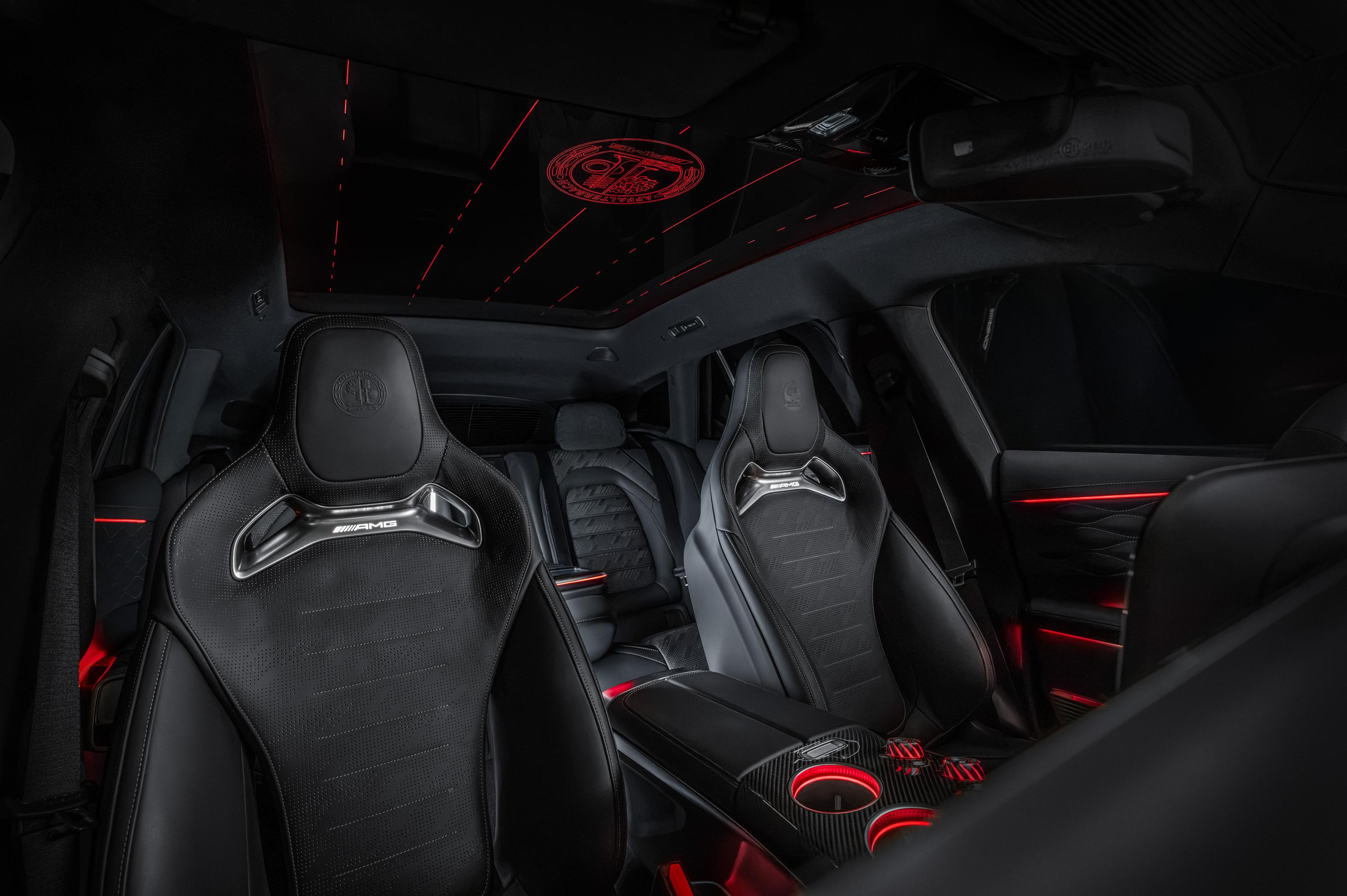 Interior de carro esportivo com bancos de couro pretos e detalhes em vermelho, incluindo iluminação ambiente no teto, portas e console central. O teto tem um emblema circular iluminado em vermelho e linhas finas que se estendem. Os bancos dianteiros possuem o logo AMG em metal prateado. O console central tem porta-copos iluminados em vermelho. O ambiente é escuro e moderno