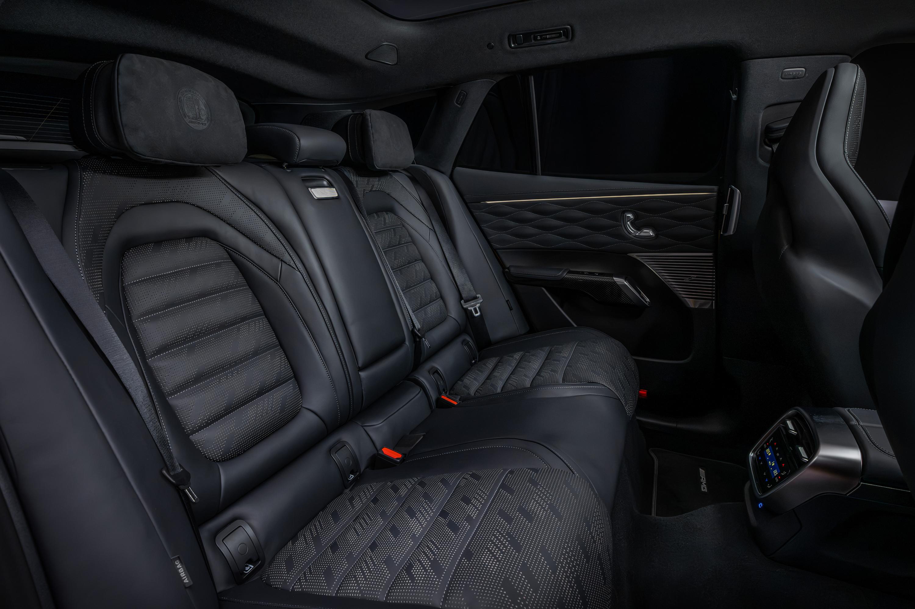 Interior de carro luxuoso com bancos traseiros de couro preto, estofamento texturizado e encostos de cabeça com emblema. Detalhes em metal e painel da porta com padrão acolchoado. Visão do banco do passageiro dianteiro e console traseiro com controles digitais