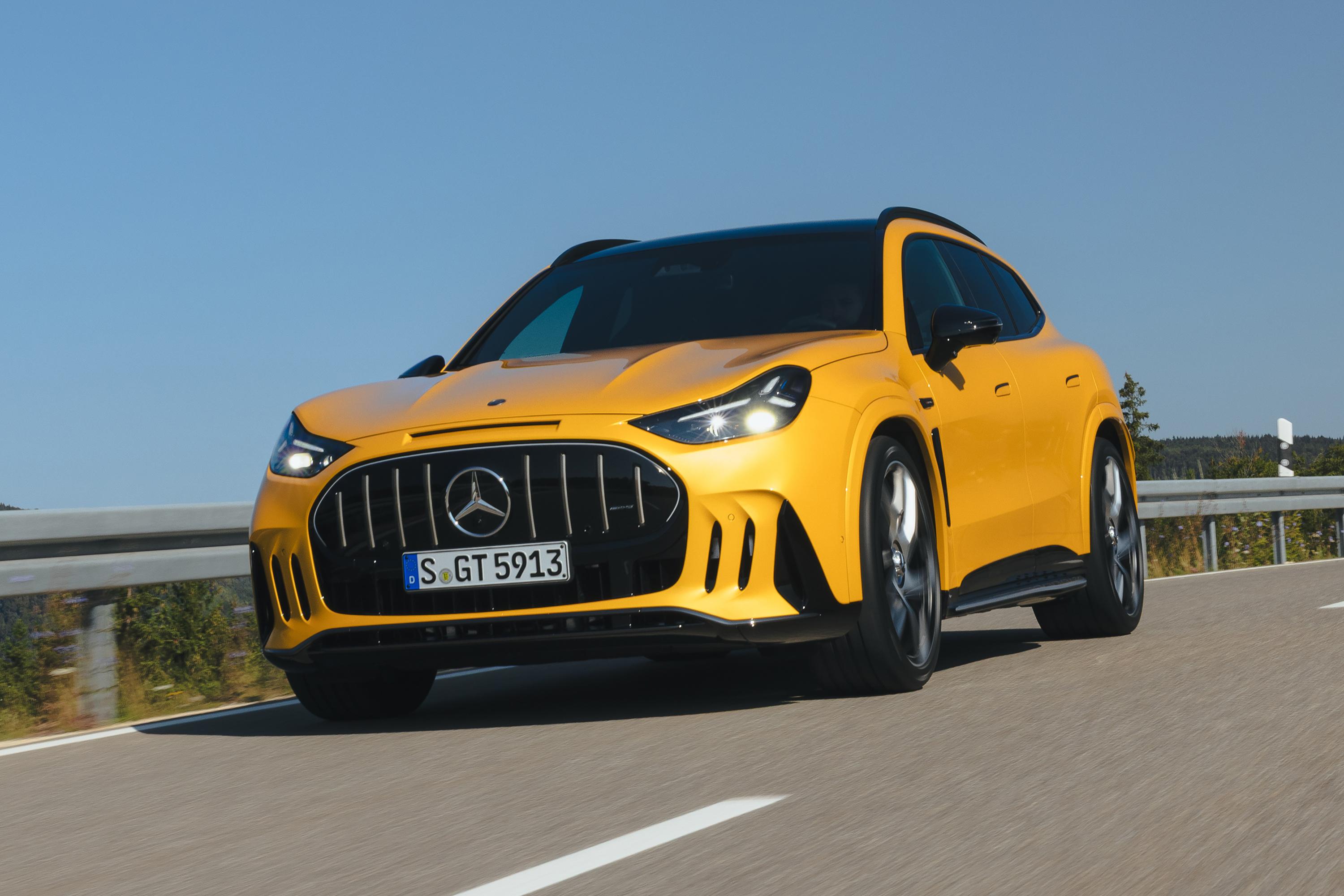 SUV Mercedes-Benz AMG GLC 63 S E Performance amarelo brilhante em movimento numa estrada asfaltada, com grade frontal preta, faróis acesos e teto escuro. O céu azul claro domina o fundo, e um guard-rail cinza metálico aparece à esquerda