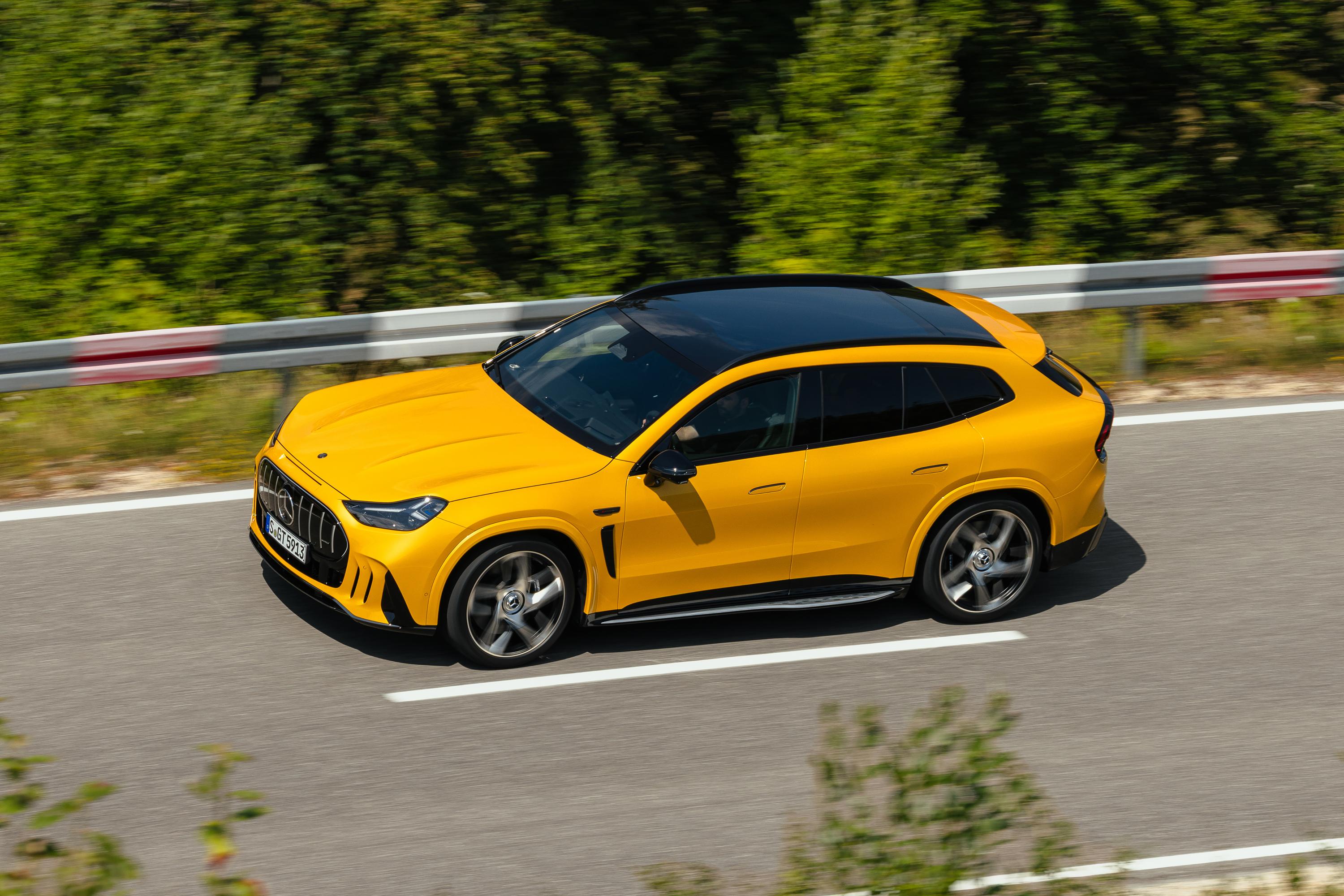 Carro SUV esportivo amarelo com teto preto, em movimento rápido, visto de cima e lateralmente, em uma estrada asfaltada com guard-rail e vegetação borrada ao fundo