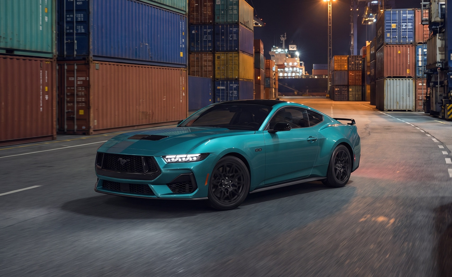 Carro esportivo Ford Mustang GT 2024 azul-turquesa com teto preto, rodas escuras e faixas no capô, parado em uma rua de porto à noite, com contêineres coloridos empilhados e um navio de carga ao fundo