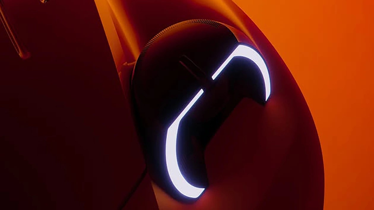 Mouse gamer preto com iluminação LED branca em formato de C na lateral e na parte superior, sobre uma superfície em tons de laranja e vermelho, com reflexos de luz