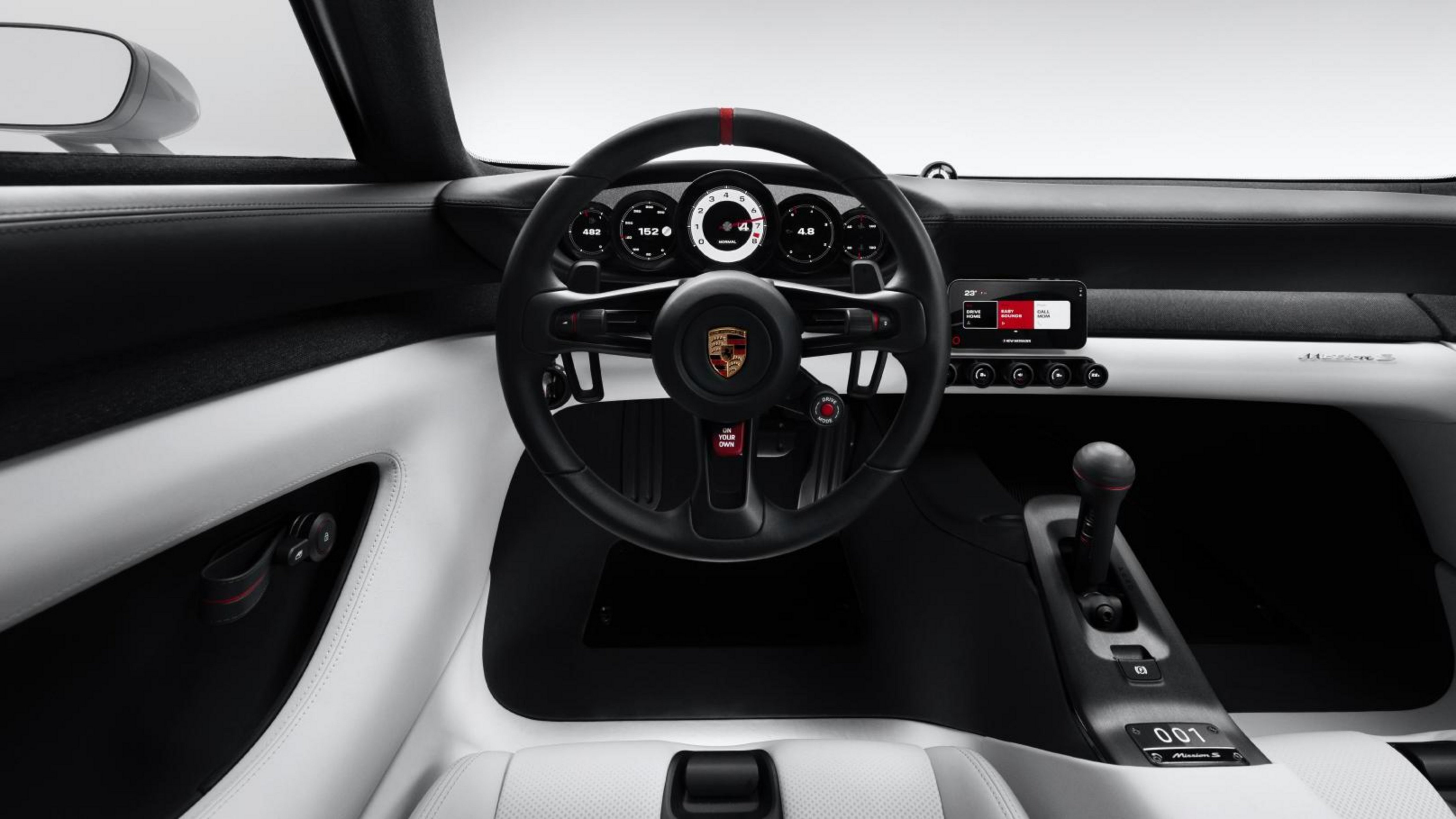 Interior de um carro esportivo Porsche, com volante preto e detalhes vermelhos, painel de instrumentos digital e tela multimídia. O estofamento é branco e preto, com câmbio manual e console central.