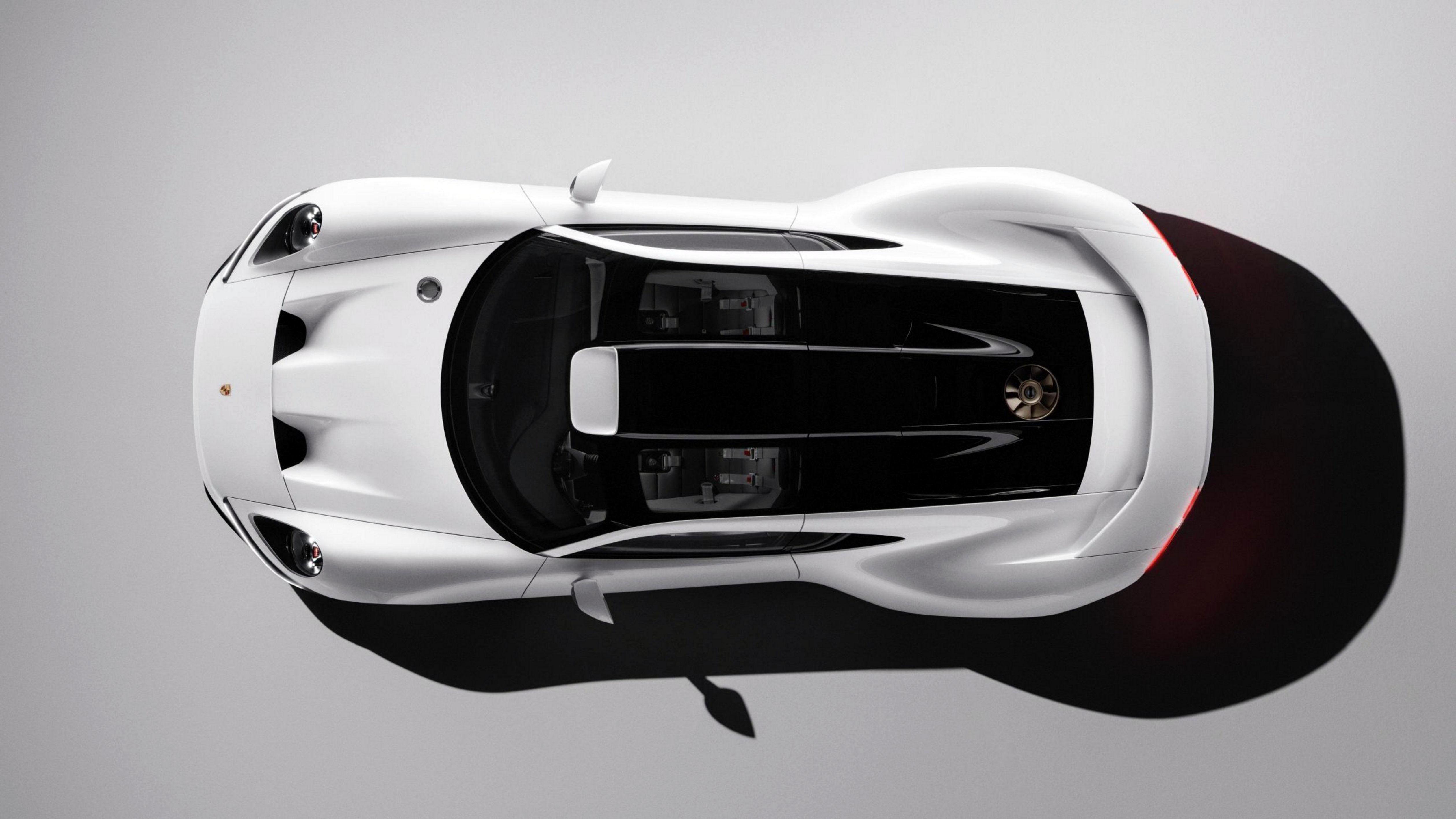 Carro esportivo branco de luxo visto de cima, com detalhes pretos no teto e motor exposto na traseira, projetando uma sombra escura no chão cinza