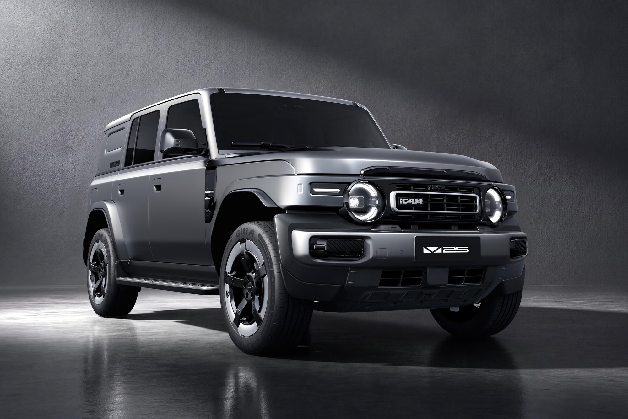 SUV cinza-chumbo com design robusto, faróis redondos acesos e grade frontal retangular, estacionado em um estúdio com piso reflexivo e parede escura