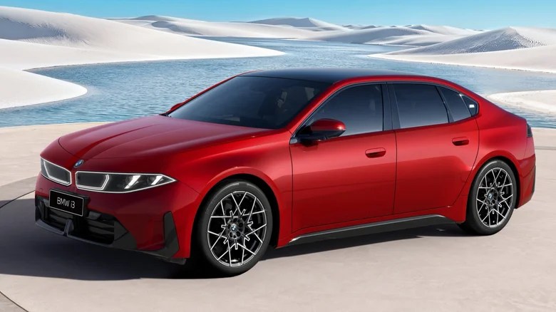 Carro BMW B vermelho com teto preto, estacionado em uma área plana, com dunas de areia branca e lagoas azuis ao fundo