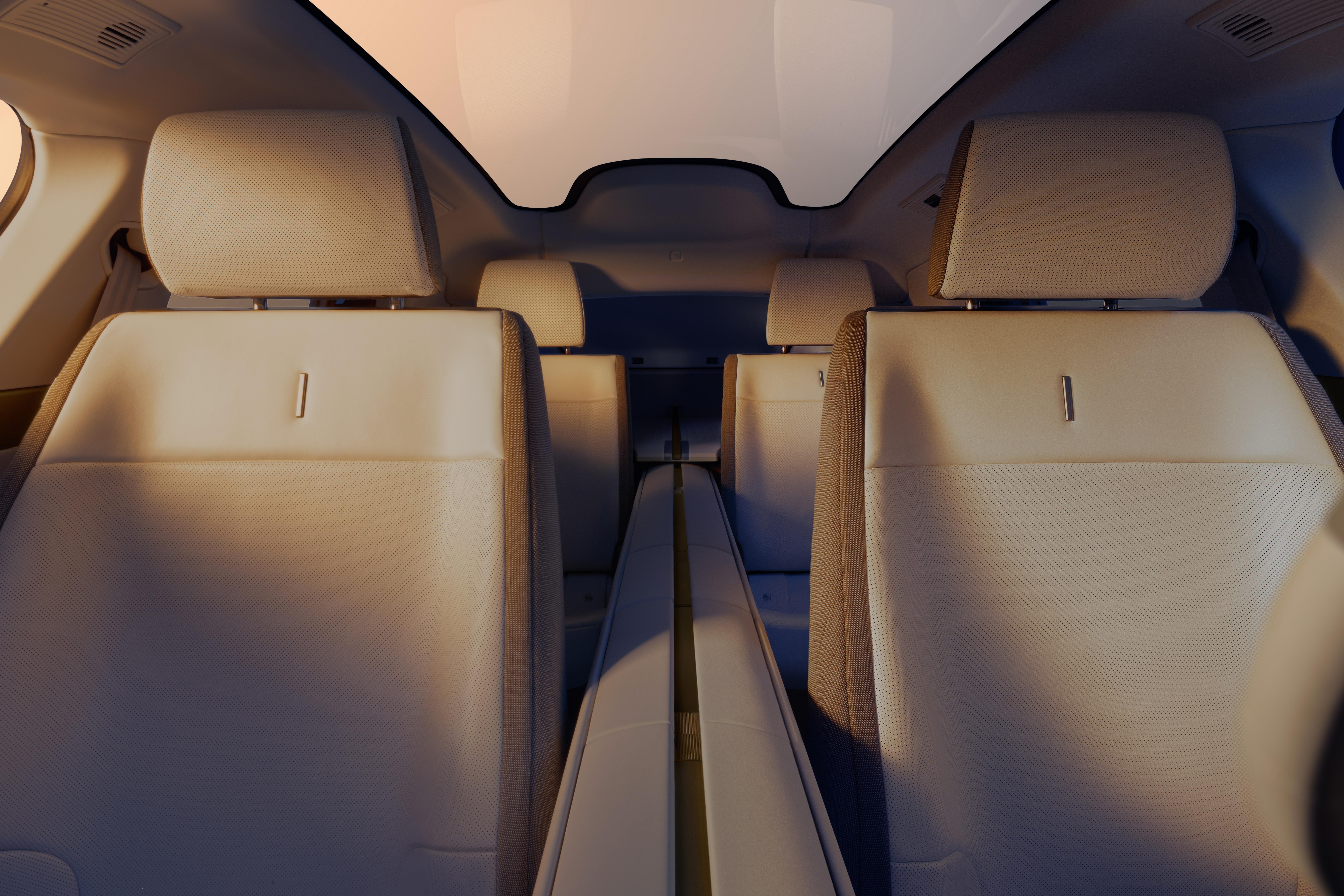 Interior de um carro com assentos de couro bege claro e encostos de cabeça, vistos de trás. Há um teto solar panorâmico e uma iluminação suave, criando um ambiente espaçoso e moderno